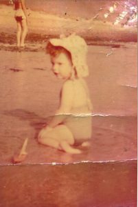 Creased, sepia photo of Julie in the sea, at two years of age.