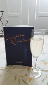 A copy of 'Identity Reclaimed: Echoes of an Adoptee' posed with a flute of bubbly on Publication Day, September 29th 2017